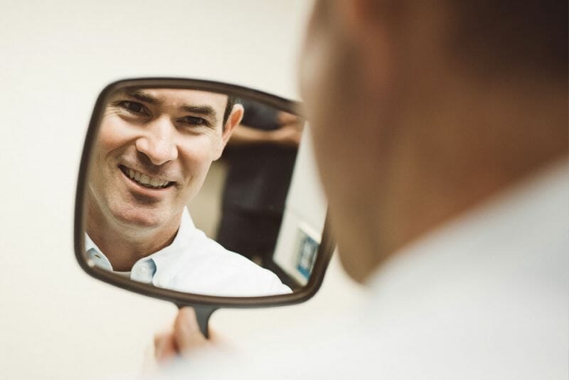 Man looking at himself in handheld mirror and smiling